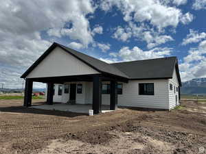 View of back of house with a mountain view, a patio, and a shingled roof