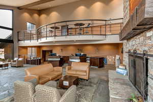 Living room with stone tile flooring, a stone fireplace, and a high ceiling