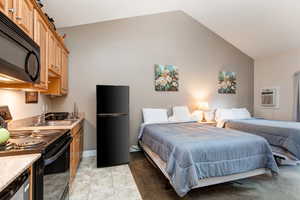 Bedroom featuring vaulted ceiling, a wall mounted air conditioner, light tile patterned floors, and freestanding refrigerator