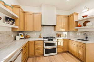 Kitchen featuring open shelves, range with two ovens, custom hood, tasteful backsplash, light wood flooring, and Quartzite countertops