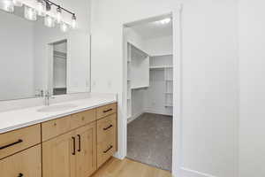 Bathroom with a walk in closet, vanity, and light wood-type flooring