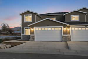 View of front of house featuring stone siding, a garage, concrete driveway, and stucco siding