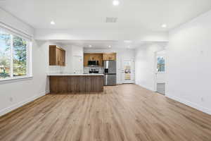 Kitchen with brown cabinetry, light countertops, appliances with stainless steel finishes, open floor plan, and a peninsula