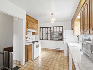 Kitchen with light countertops, white appliances, light flooring, a chandelier, and under cabinet range hood