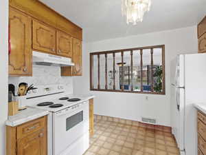 Kitchen featuring white appliances, light countertops, brown cabinets, and under cabinet range hood