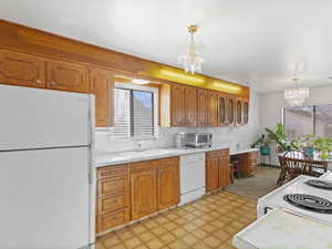 Kitchen with white appliances, a chandelier, light countertops, brown cabinetry, and light flooring