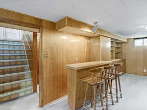 Indoor dry bar with light carpet, wooden walls, and stairs