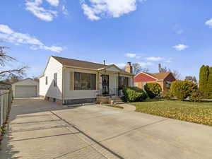 Bungalow featuring an outbuilding, a detached garage, driveway, a front yard, and a chimney