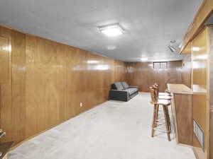 Basement living room featuring wood walls and light carpet