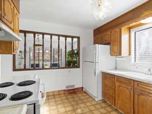 Kitchen with brown cabinets, white appliances, light countertops, light flooring, and under cabinet range hood