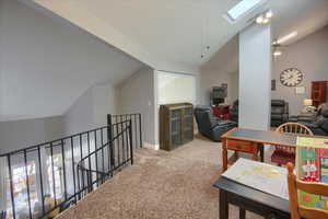 Corridor featuring vaulted ceiling, a skylight, light colored carpet, and an upstairs landing