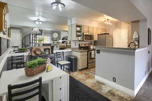 Kitchen with a breakfast bar area, stainless steel appliances, a peninsula, a chandelier, and dark stone counters