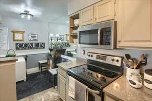 Kitchen with stainless steel appliances, open shelves, and light stone countertops