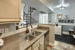 Kitchen with stainless steel dishwasher, cream cabinets, light stone countertops, and a peninsula