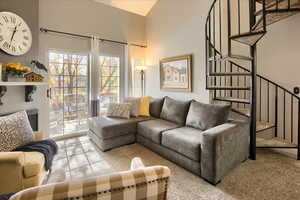Living room with stairs, light carpet, and a high ceiling