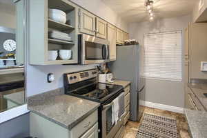 Kitchen featuring appliances with stainless steel finishes, open shelves, light stone counters, and stone tile floors