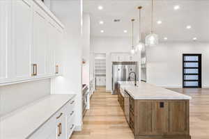 Kitchen with white cabinetry, light wood-style floors, light stone countertops, a large island with sink, and hanging light fixtures