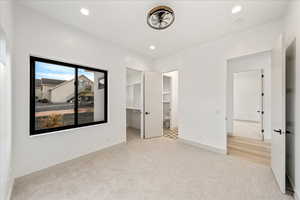 Unfurnished bedroom featuring light carpet, a spacious closet, ensuite bath, and recessed lighting
