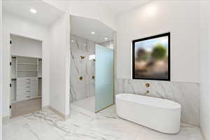 Full bath with marble tiled flooring, a walk in closet, a freestanding tub, recessed lighting, and a marble finish shower