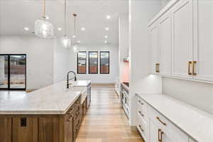 Kitchen with white cabinetry, light stone counters, hanging light fixtures, light wood-style floors, and a spacious island