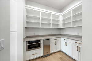 Kitchen featuring light wood-style floors, white cabinets, stainless steel appliances, including a wine fridge and light stone counters