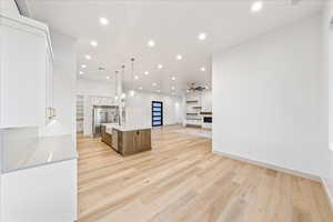 Kitchen featuring open floor plan, decorative light fixtures, white cabinets, a kitchen island with sink, and recessed lighting