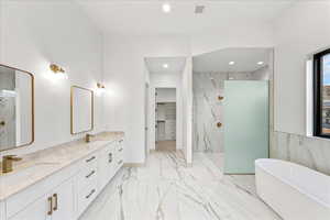 Bathroom with a walk in closet, a marble finish shower, a freestanding tub, double vanity, and recessed lighting