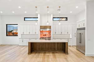 Kitchen with lux appliances, white cabinetry, built in refrigerator, decorative light fixtures, an island with sink, and recessed lighting