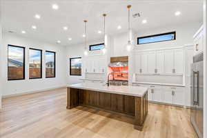 Kitchen featuring white cabinetry, a center island with sink, decorative light fixtures, built in fridge, and recessed lighting
