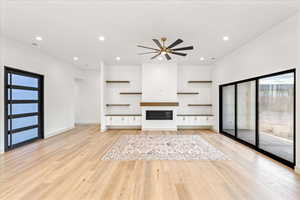 Unfurnished living room with plenty of natural light, a glass covered fireplace, light wood-style flooring, and recessed lighting