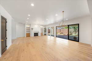 Unfurnished living room with a chandelier, a fireplace, and light wood-type flooring