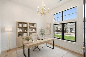 Office area featuring light wood-style floors, a high ceiling, and a chandelier