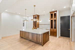 Kitchen featuring brown cabinets, a center island with sink, pendant lighting, light wood-type flooring, and recessed lighting