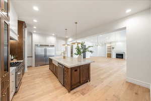 Kitchen with two tone cabinetry, a center island with sink, open floor plan, premium appliances, and light wood finished floors