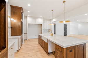 Kitchen featuring brown cabinets, light wood-type flooring, recessed lighting, white cabinetry, and a large island