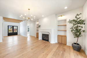 Unfurnished living room with built in features, french doors, light wood finished floors, hanging lights, and a glass covered fireplace