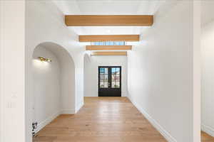 Entryway featuring french doors, arched walkways, light wood-style flooring, and beam ceiling