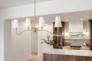 Kitchen with hanging light fixtures, light wood finished floors, light stone countertops, backsplash, and glass insert cabinets