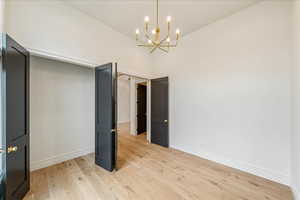 Unfurnished bedroom featuring light wood-style floors, a chandelier, and a towering ceiling