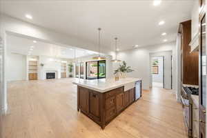 Kitchen with dark wood finish cabinets, light wood-type flooring, a fireplace, hanging light fixtures, and a center island with sink