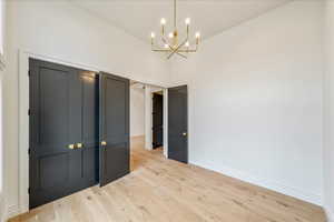 Unfurnished bedroom with wood finished floors, a towering ceiling, a closet, and a chandelier
