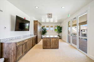 Kitchen featuring light colored carpet, brown cabinets, a kitchen island, light stone countertops, and recessed lighting