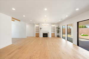 Unfurnished living room with hanging lights, a fireplace, light wood-style floors, and built in shelves