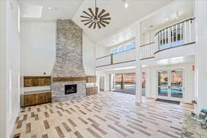 Unfurnished living room with french doors, high vaulted ceiling, a fireplace, light wood-style flooring, and recessed lighting
