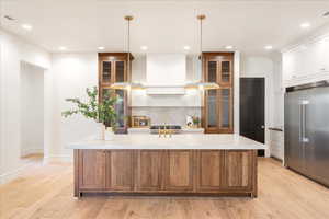 Dual tone kitchen with two tone cabinetry, built in refrigerator, decorative light fixtures, a spacious island, and light wood-type flooring