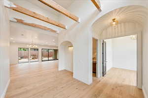 Hall featuring a chandelier, light wood finished floors, arched walkways, recessed lighting, and beam ceiling