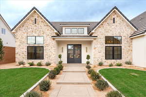 View of front of home featuring stone siding, a front yard, and covered porch