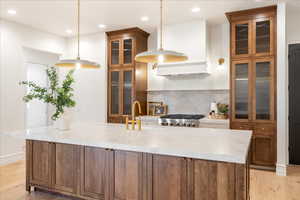 Dual tone kitchen featuring glass fronted cabinets, light wood finished floors, pendant lighting, tasteful backsplash, and dual tone cabinets