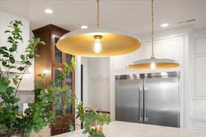 Kitchen with stainless steel built in fridge, glass fronted cabinets, decorative light fixtures, white cabinetry, and light stone counters