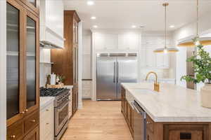 Two tone kitchen featuring two tone color scheme, high end appliances, glass fronted cabinets, decorative light fixtures, and light stone countertops